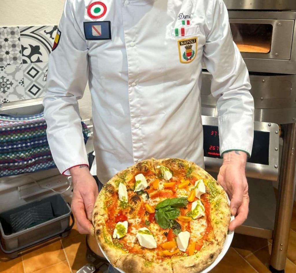 Le pizzaïolo en veste de cuisine, présentant une pizza à la sortie du four