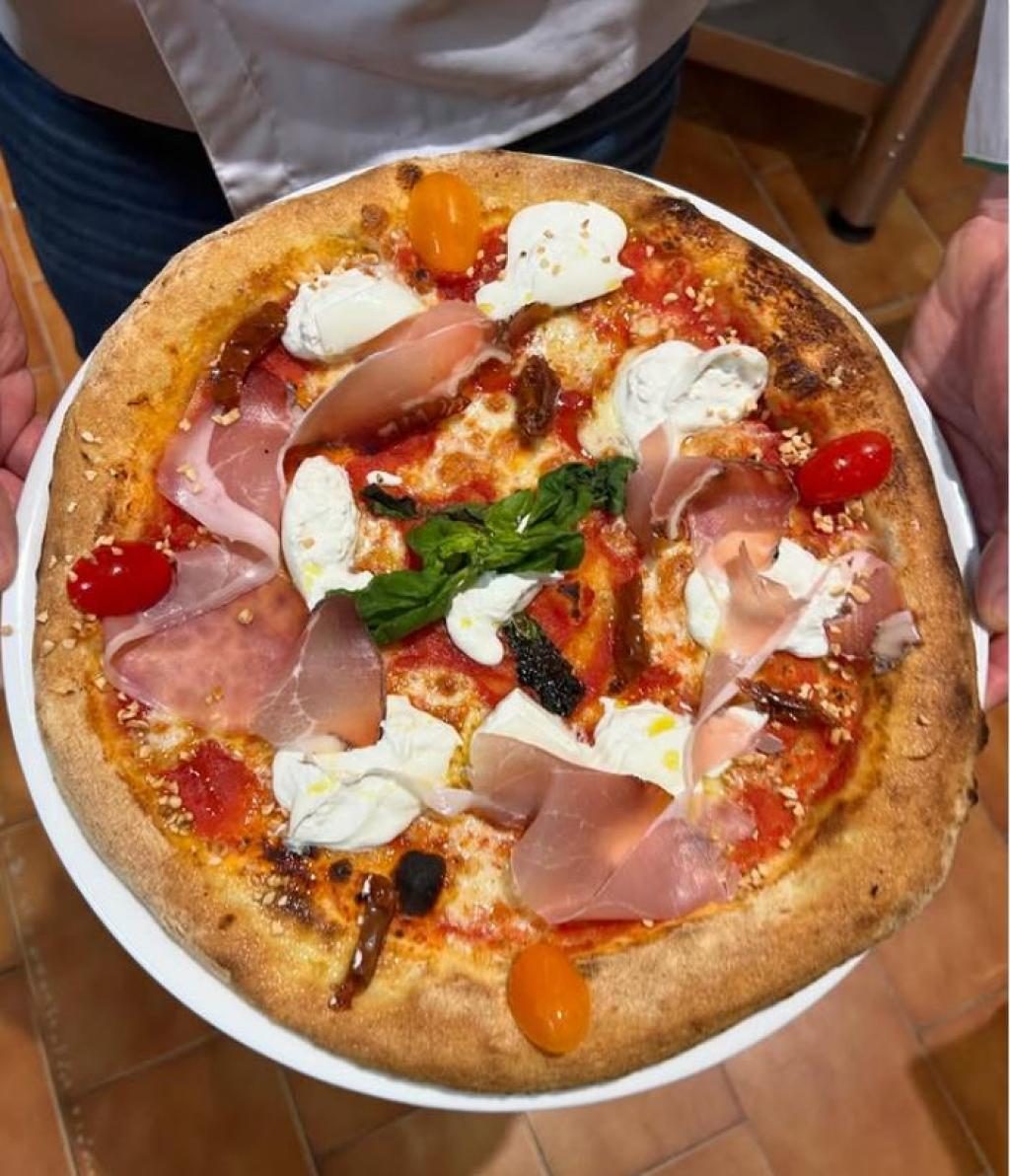 Une pizza au jambon, parmesan et herbes, cuite à point